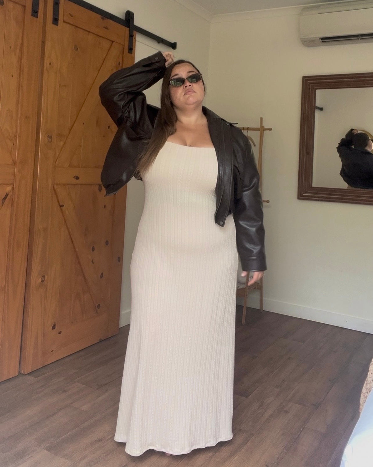 Model wearing Delilah Knitted Dress in cream, square neckline ribbed knit maxi dress, styled with brown leather jacket and sunglasses, indoor barn door setting