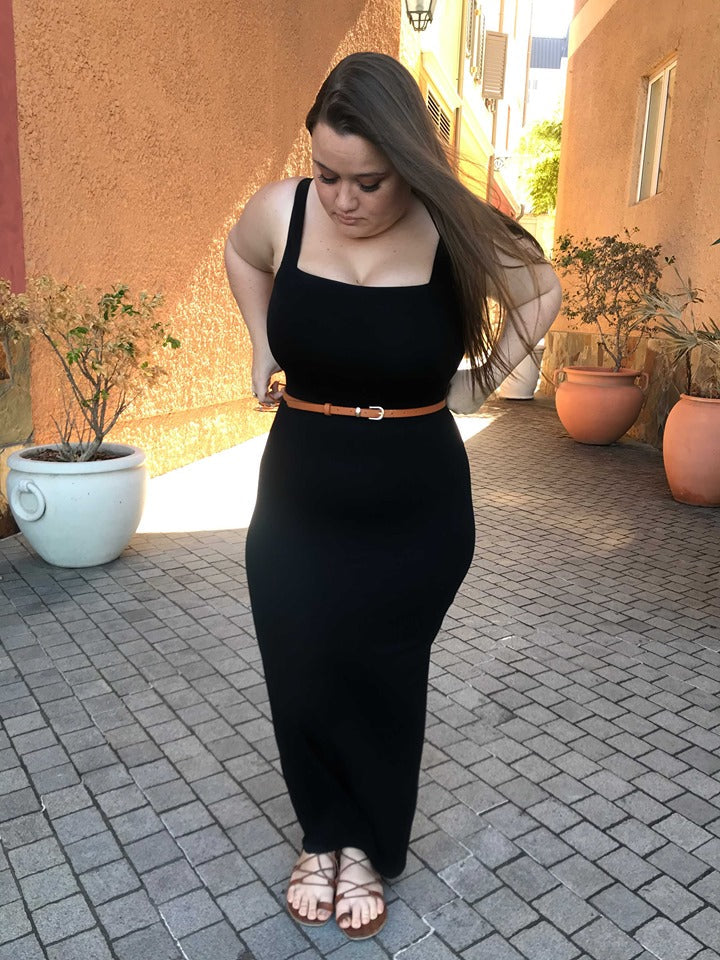 Model in black square-neck Audrey Dress - Long with tan belt, walking through a cobblestone alley