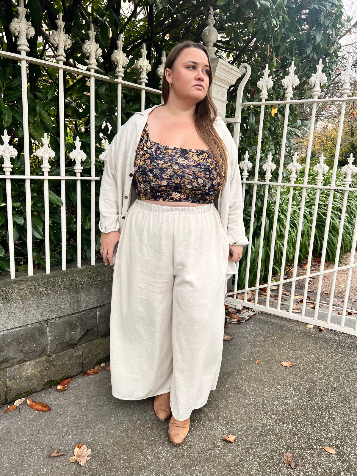 Model in cream wide-leg Charlie Pants with floral crop top and open shirt, iron gate background