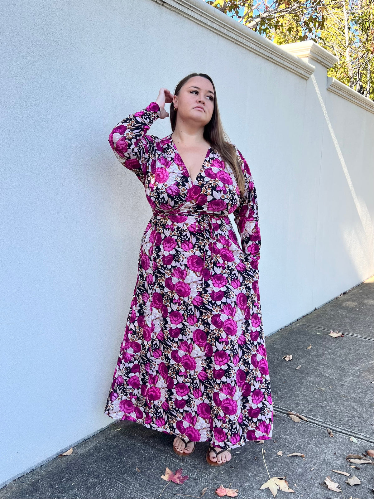 Model wearing Alexia Wrap Dress in Pink Rose print, long sleeve V-neck wrap maxi dress in magenta and black floral, against white wall