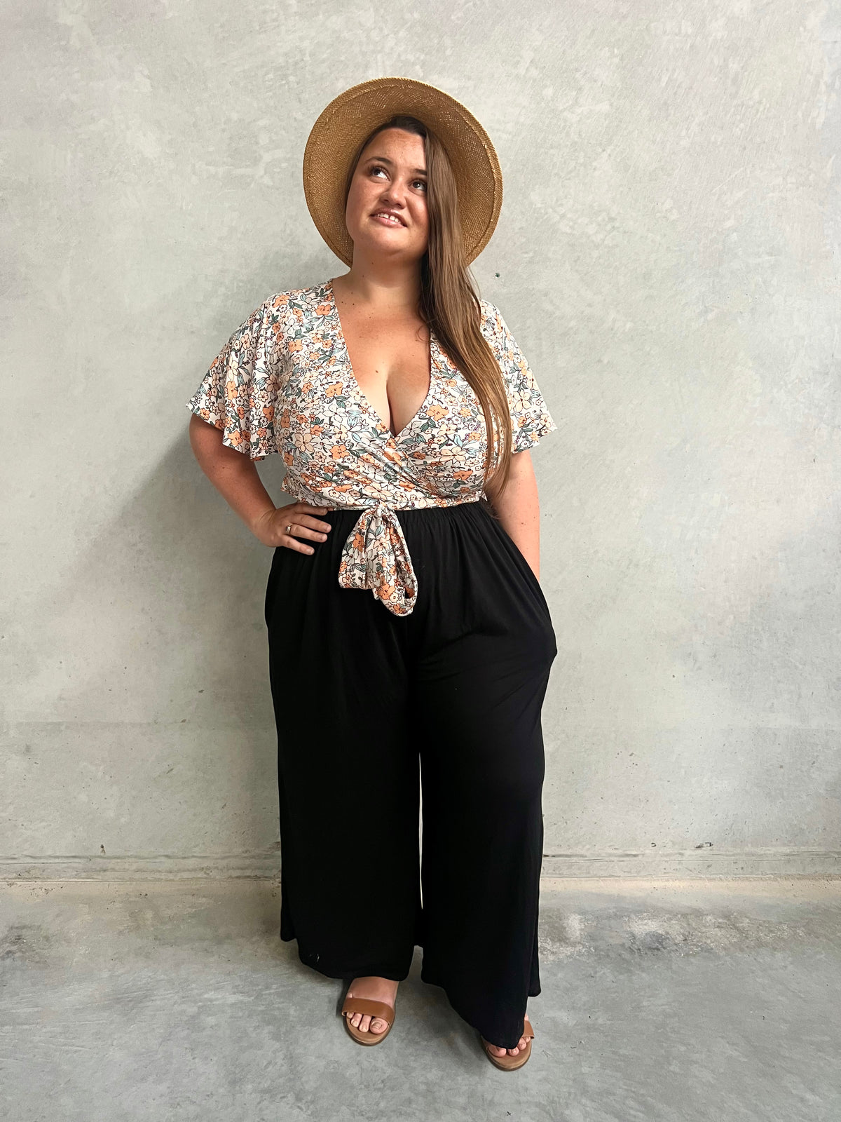 Model in black wide-leg Vivienne Pants styled with a floral wrap top and straw hat